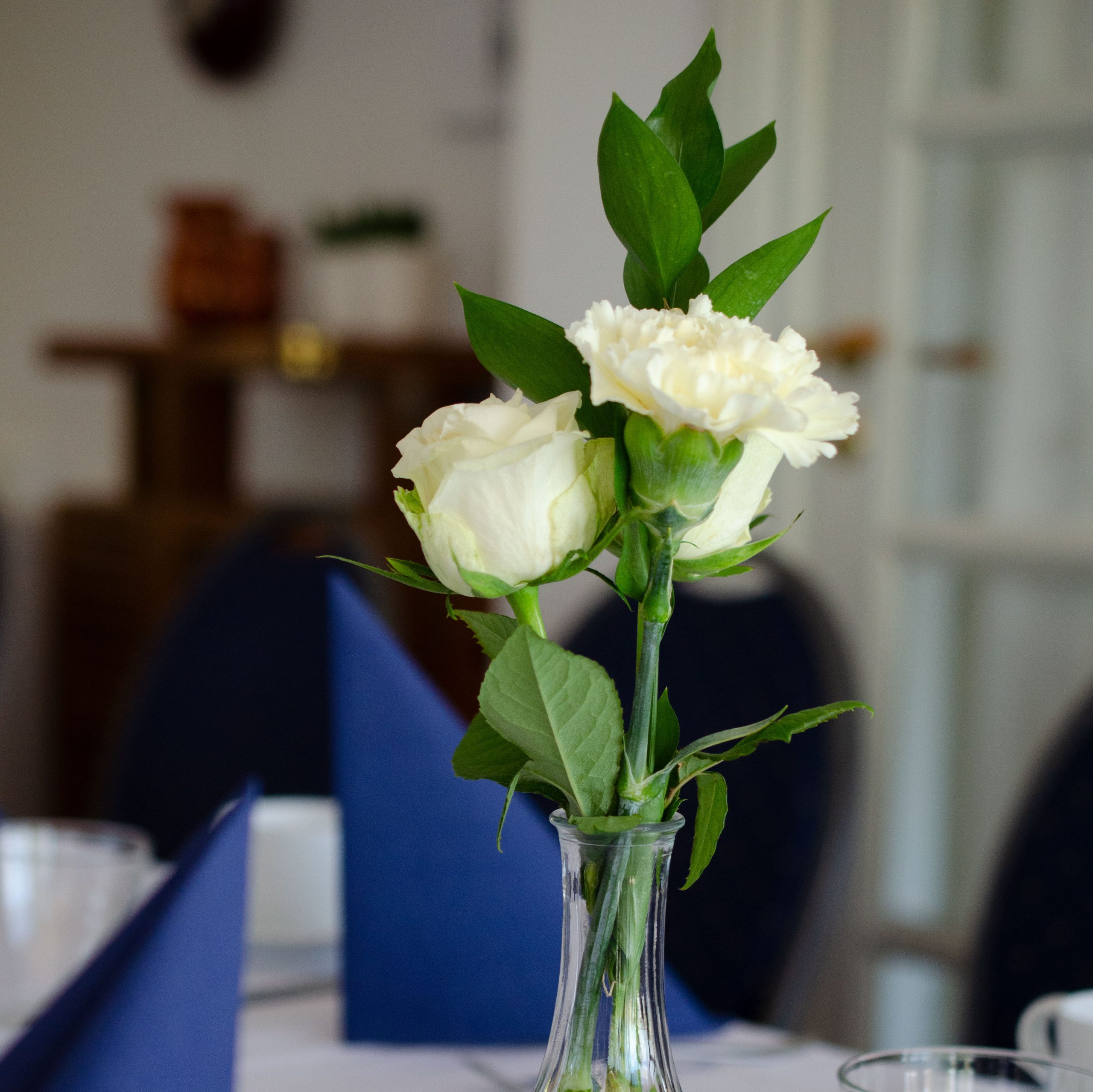 Bord dækket på med kaffekopper, blå servietter og hvide roser.